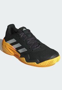 Černá sportovní bota s síťovaným svrškem, třemi stříbrnými pruhy a texturovanou oranžovou podrážkou. Má polstrovaný límec a systém šněrování.