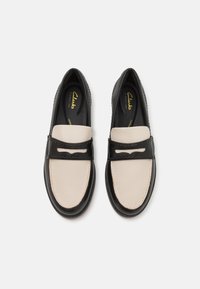 Chaussures en cuir noir et crème à enfiler avec une finition lisse et des accents cousus. Design profil bas avec un bout rond. Semelle légère.