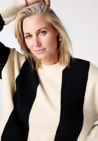 Gebreide trui met oversized zwarte en crèmekleurige strepen, een ronde halslijn en een losse pasvorm. Zachte textuur met een comfortabele vorm.