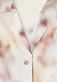 Lagani pamučni laneni top sa ovratnikom s urezom, jednim vidljivim gumbom i mekim, zamagljenim uzorkom tie-dye u ružičastim, narančastim i bež nijansama.