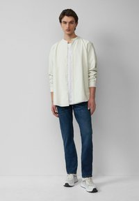 Witte en groene gestreepte shirt met een bandkraag, met knopen aan de voorkant. Draagt over een wit shirt en gecombineerd met donkerblauwe jeans en sneakers.