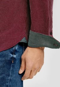 Bordowa koszula w kratę z szarymi deninowymi mankietami; posiada zaokrąglony dół i zapięcie na guzik na mankiecie, prezentując teksturowany wzór.