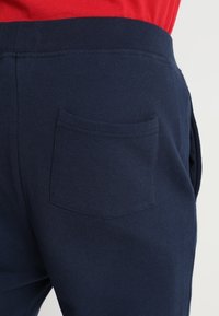 Navyblauwe katoenen broek met een achterzak en een elastische tailleband. Soepele textuur met gestikte details aan de rand van de zak.