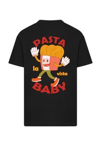 Melnas kokvilnas T-kreklā, kurā attēlots karikatūras varonis ar makaronu krūzē, sarkans teksts "PASTA BABY" un "la vista", kā arī oranžas akcents uz apaviem.