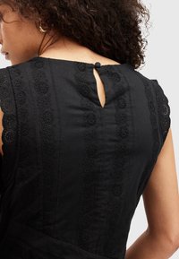 Vestido de algodón negro con un escote redondo tipo ojal en la parte trasera y cierre de botón, bordado de ojetes y detalles en forma de ondas a lo largo de las costuras.