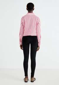 Chemise à manches longues rayée rouge et blanche, leggings noirs, et chaussures plates à motif léopard ; avec un col classique et des poignets boutonnés.