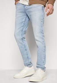 Ljust blå denimjeans med slim fit, som har en urtvättad look och subtila slitningar, ihopparat med vita sportskor.