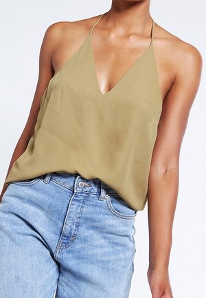 Oliwkowy bezrękawnik z głębokim dekoltem w kształcie litery V i cienkimi ramiączkami, w połączeniu z jasnoniebieskimi spodniami z wysokim stanem. Gładka tekstura materiału.
