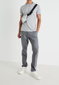 T-shirt grigia in cotone abbinata a pantaloni grigi chiari, completata da una borsa a tracolla argentata e sneakers bianche con una superficie liscia.