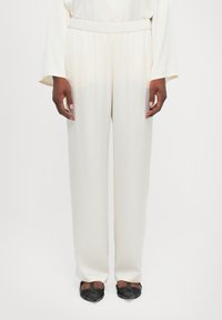 Pantalones sueltos de color crema con cintura elástica. Tejido suave con un sutil brillo, combinados con zapatos negros de punta.