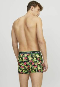 Boxer-briefs noirs avec un motif floral tropical comprenant des feuilles vertes, des fleurs roses et jaunes, ainsi qu'une ceinture noire contrastante portant le nom de la marque.