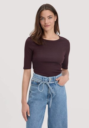 Burgunderfarbener taillierter Oberteil mit kurzen Ärmeln, rundem Halsausschnitt, kombiniert mit hochgeschnittenen hellblauen Jeans und einem gebundenen Gürtel. Glatte Textur.
