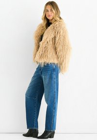Beige faux fur cropped jacket with a shaggy texture, paired with loose blue jeans and black ankle boots. Simple black top underneath.