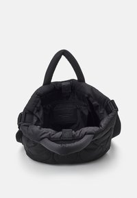 Sac noir matelassé avec une texture de tissu doux, présentant une large ouverture, une poche zippée intérieure et une bandoulière amovible.