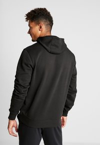 Sudadera con capucha negra de textura suave, con puños y dobladillo de canalé. La capucha es prominente y el diseño es simple y casual.