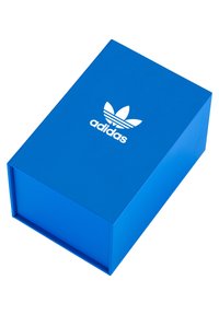 Modrá obdlžníková obalová krabica s textúrovaným povrchom a bielym logom Adidas na vrchu, ktoré zobrazuje klasický dizajn s tromi listami.