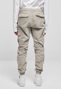 Beige Cargo-Hosen mit elastischen Bündchen, flachen Gesäßtaschen und Seitentaschen. Kombiniert mit weißen Sneakern und einem Langarmhemd.