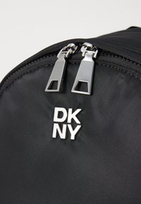 Black nylon backpack featuring dual silver zipper pulls and a prominent embossed DKNY logo on the front. Smooth texture with matte finish.