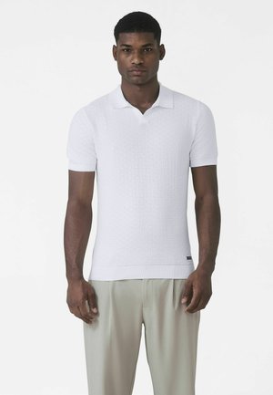 Valge lühikeste varrukatega polosärk tekstuurse mustriga, kraega kaelus, soonikkoes varrukasääred ja alläär. Sobitatud heledate, lahtiste pükstega.