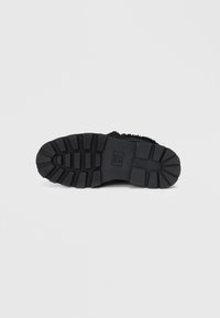 Suela de zapato de goma negra con un dibujo profundo, que presenta ranuras horizontales y verticales, y un logo grabado en el centro.