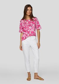 Short-sleeve top with pink floral pattern on white background. Paired with white slim-fit pants and light brown sandals. Smooth fabric texture.