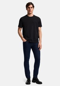 Maglietta nera a girocollo, jeans attillati blu scuro e scarpe nere stringate. Materiale in cotone morbido, design minimalista e palette di colori neutri.