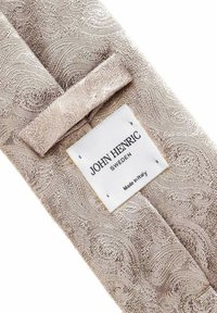 Ljusbeige tyg med paisleymönster och en vit rektangulär etikett med texten "John Henric Sweden Made in Italy" sydd på.