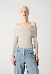 Beige avskjørt ribbet topp med lange ermer og teksturert stoff, kombinert med lyseblå vide jeans med klassiske lommer.