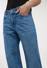 Jasnoniebieskie dżinsy o luźnym kroju, z pięcioma kieszeniami, szlufkami na pasek oraz metalowym zapięciem na brzegu pasa.