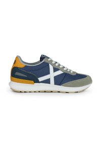 Zapatilla deportiva en azul marino y gris con toques blancos, hecha de materiales de ante y tela, con lengüeta separada y suela de goma; cuenta con un detalle en amarillo en el talón.