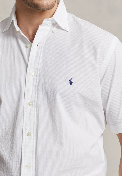 White button-up shirt with a ribbed texture, short sleeves, and a small blue polo logo on the chest. Includes pearl-like buttons.