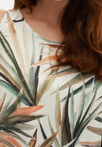 Tissu à motif floral avec des feuilles vertes, beiges et orange sur un fond clair, présentant une texture lisse et une drape douce.