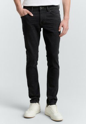 Jean slim noir avec poches avant et fermeture à bouton. Porté avec des baskets blanches, présentant une texture de tissu lisse.