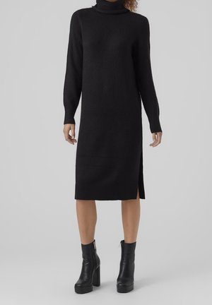 Musta neulekaulusmekko, jossa on pitk�ät hihat, polvipituus, sivuavoin yksityiskohta ja ribbaushelma, yhdistettynä mustiin platform nilkkakorkoihin.
