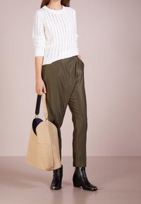 Pull en maille blanche avec des motifs ajourés, pantalon olive vert fuselé, bottines noires et sac à main en daim beige avec une forme incurvée.