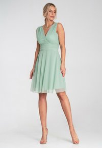 Ein hellgrünes Chiffonkleid mit V-Ausschnitt, gerafftem Oberteil und schw flowy Rock. Es hat einen ärmellosen Schnitt und einen geschichteten Saum.