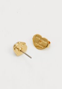 Guld hjärtformade studs med en slät finish, prydda med en liten ädelsten och graverat varumärke på baksidan.
