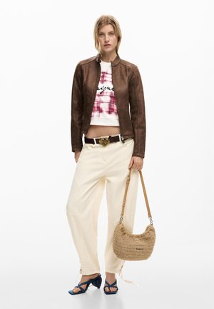 Vrouw met een bruine leren jas, wit en rood grafisch cropped topje, crème wijde broekspijpen, blauwe sandalen met hak, en een beige gevlochten schoudertas.