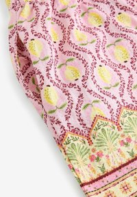Tissu rose avec motif répété de fruits jaunes, vignes feuillues bordeaux et bordure florale verte.