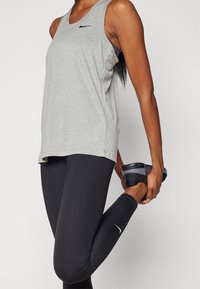 Szary sportowy top bez rękawów z małym czarnym logo, w połączeniu z czarnymi legginsami z białym logo, odpowiedni do aktywności sportowych.