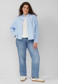 Lichtblauw en wit gestreept overhemd met knopen over een wit topje, gecombineerd met blauwe jeans en witte sneakers. Casual, ontspannen pasvorm.
