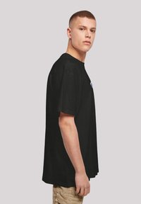 Black crew neck t-shirt with short sleeves, straight cut, made of cotton fabric, featuring a small graphic on the front and a smooth texture.