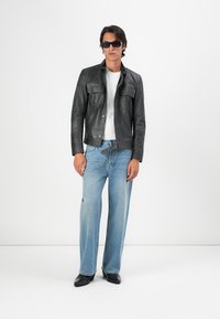 Chaqueta de cuero negra con bolsillos frontales, combinada con una camiseta blanca y unos jeans de pierna amplia azul claro. El calzado consiste en botas negras elegantes.