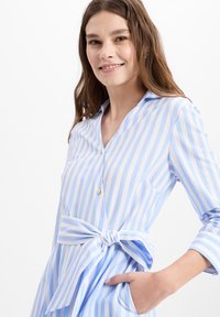 Light blue and white striped dress with a button front, collar, long sleeves, and a tied waist belt. Features side pockets and a smooth texture.