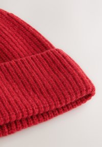 Red knitted beanie featuring ribbed texture, thick fabric, and a folded cuff design for warmth and comfort.