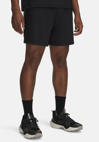 Schwarze Cargo-Shorts aus leichtem Stoff, mit Seitentaschen und lockerer Passform. Getragen mit schwarzen Sneakers und Kniestrümpfen.
