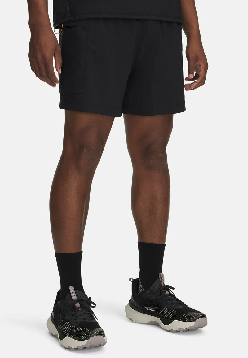 Schwarze Cargo-Shorts aus leichtem Stoff, mit Seitentaschen und lockerer Passform. Getragen mit schwarzen Sneakers und Kniestrümpfen.