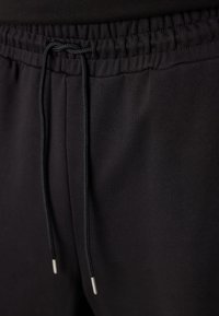 Schwarze Jogginghosen mit einer Kordelzug Taille. Mit elastischem Bund und Kordelzug mit silbernen Spitzen. Leicht strukturierten Stoff.
