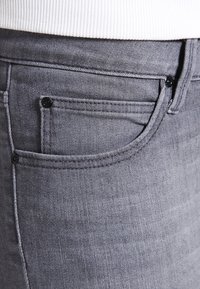 Los jeans de mezclilla gris presentan un diseño clásico con un estilo de cinco bolsillos, herrajes negros en contraste y una textura suave.