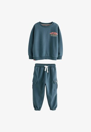Plavi dječji dukserica s natpisom "Superdry Outdoor" u kombinaciji s odgovarajućim cargo jogger hlačama s bijelim vezicom.